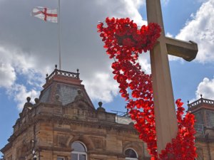 The poppy decorated cross plus flag at half mast on the Town Hall.